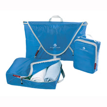 Load image into Gallery viewer, A set of three blue Eagle Creek Pack-It Specter organizers, including a medium-sized folder, a cube, and a half-cube, laid out with zippered compartments opened and filled with clothes.
