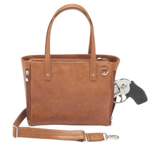 Load image into Gallery viewer, Front view of the tan leather concealed carry purse with a gun peeking from the compartment. The adjustable shoulder strap is removed and laid at the front.
