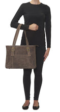 Load image into Gallery viewer, A young woman dressed in black holds the tan leather bag with the shoulder straps on her forearm.
