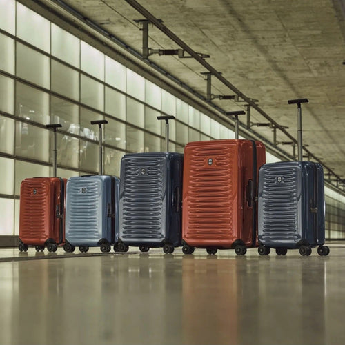 A red, light blue, medium navy blue, orange, and carry-on-sized navy blue suitcase grouping lined up on an urban setting. 