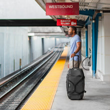 Load image into Gallery viewer, A man holding the duffel bag while waiting at a train station.
