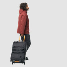 Load image into Gallery viewer, A young man pulling his suitcase behind him by the telescopic handle on a white background. 
