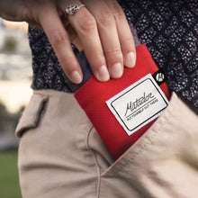 Load image into Gallery viewer, A person pulling the folded red blanket from their pants' pocket.
