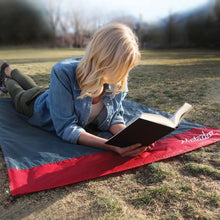 Load image into Gallery viewer, A young woman laying down on the blanket while reading a book outside.

