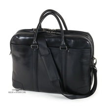 Load image into Gallery viewer, Angled front view of the black suitcase with the shoulder strap draped across it. 
