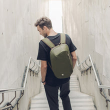 Load image into Gallery viewer, A young man standing on a flight of stairs while carrying the green backpack. 
