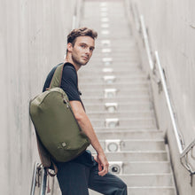 Load image into Gallery viewer, A young man standing on a flight of stairs while carrying the green backpack. 
