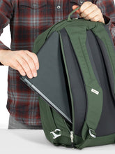 Load image into Gallery viewer, A young man sliding a laptop into the green backpack's back panel compartment.
