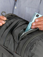 Load image into Gallery viewer, Close up to the top panel of the backpack with a phone being placed in the compartment.
