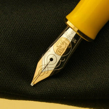 Load image into Gallery viewer, A gold-plated fountain pen nib with a yellow grip section featuring intricate designs on the barrel. 
