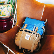 Load image into Gallery viewer, The blue and khaki backpack set on a leather chair. 
