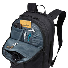 Load image into Gallery viewer, Front panel view of the black backpack with the front pocket filled with accessories. 

