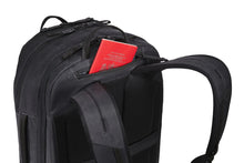 Load image into Gallery viewer, Angled back panel view of the black backpack. A red passport is tucked inside the pocket above the shoulder straps.
