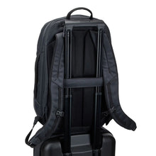 Load image into Gallery viewer, Angled back panel view of the black backpack&#39;s attachment strap holding on to the extended handle of a suitcase. 

