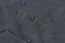 Load image into Gallery viewer, Close up to the Thule logo on the front panel with water droplets sprinkled around it, showing its waterproof fabric.
