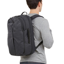 Load image into Gallery viewer, A young man facing into the background while carrying the black backpack on his back. 
