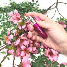 Load image into Gallery viewer, The hot pink perfume bottle held by a hand in a flowery background. 
