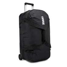 Load image into Gallery viewer, Angled front panel view of the black wheeled duffle bag. The Thule logo is printed on the front panel. 

