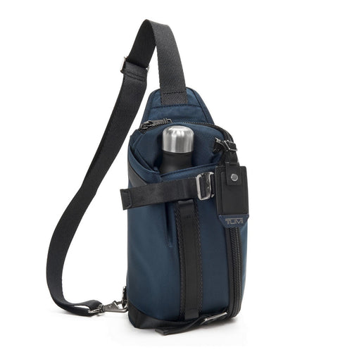 Front panel view of the Navy Blue sling bag with a water bottle shown in the adjustable front pocket. (Water bottle not included).