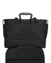 Load image into Gallery viewer, Back panel view of the bag with a suitcase&#39;s telescopic handle passing through the back strap, holding the bag in place.
